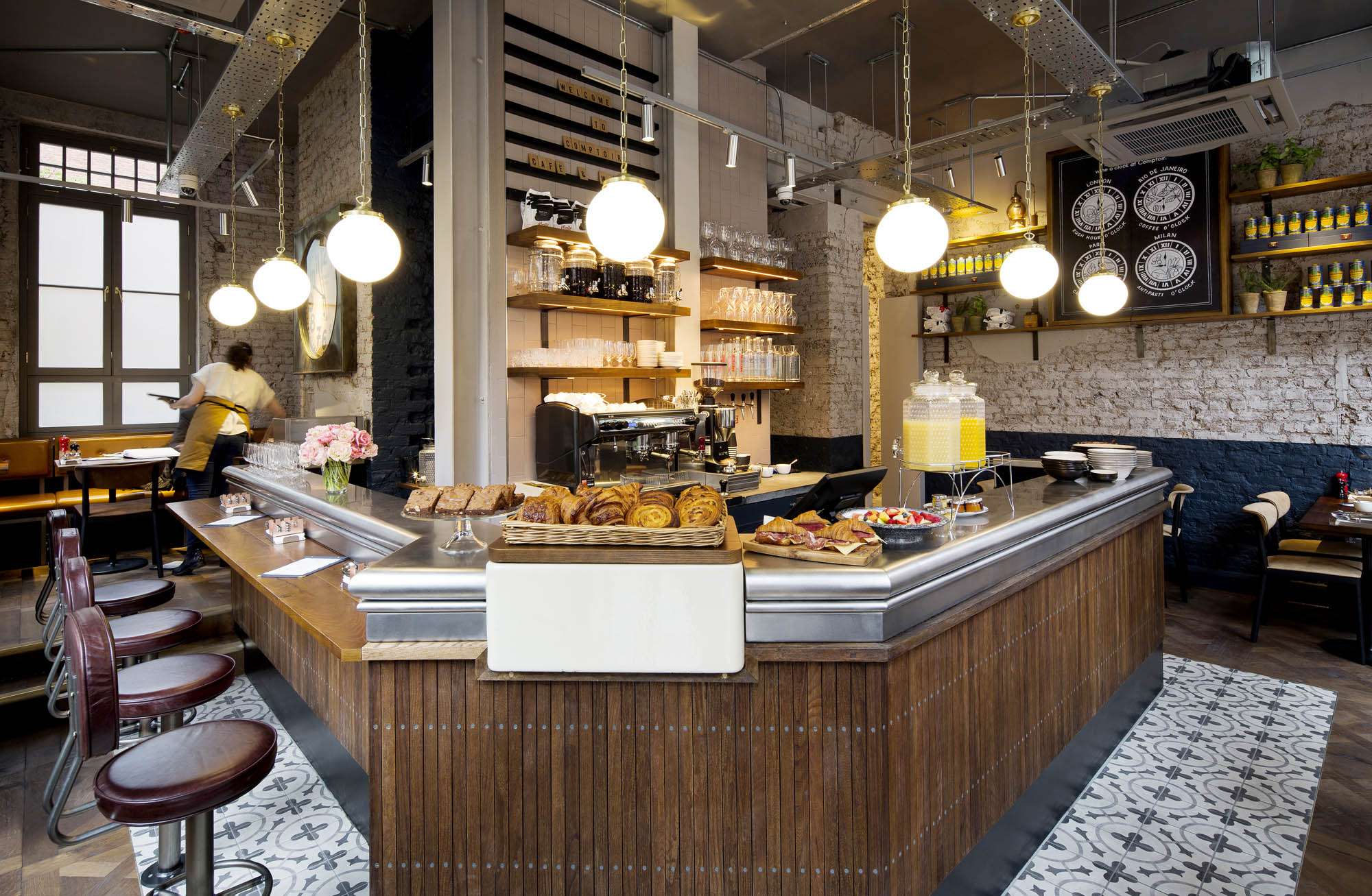 The corner coffee bar at Comptoir, with pastries on the zinc counter and globe pendants above