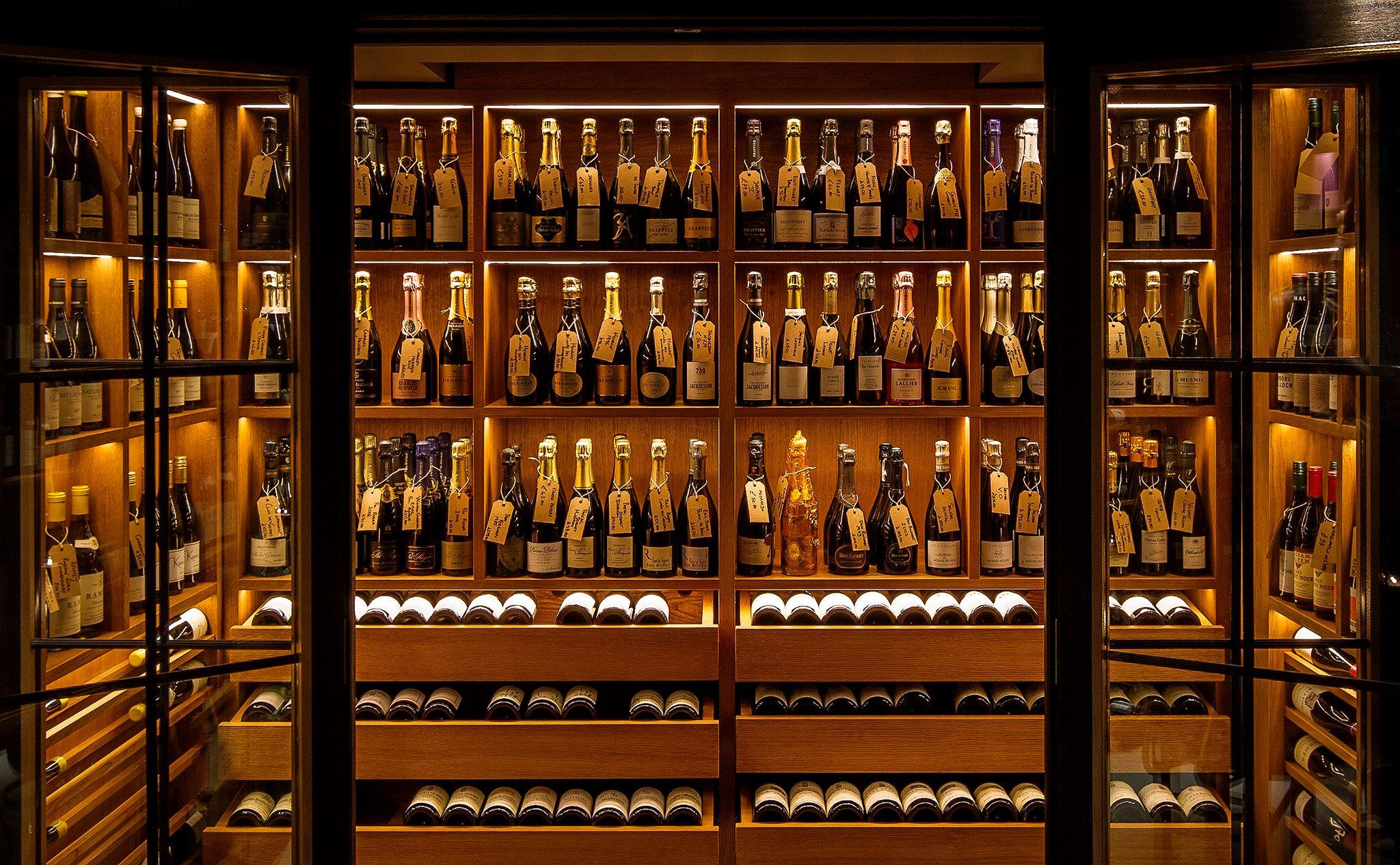 The Champagne room downstairs at Comptoir: lit oak shelves of bottles with handwritten tags, seen through open glass doors