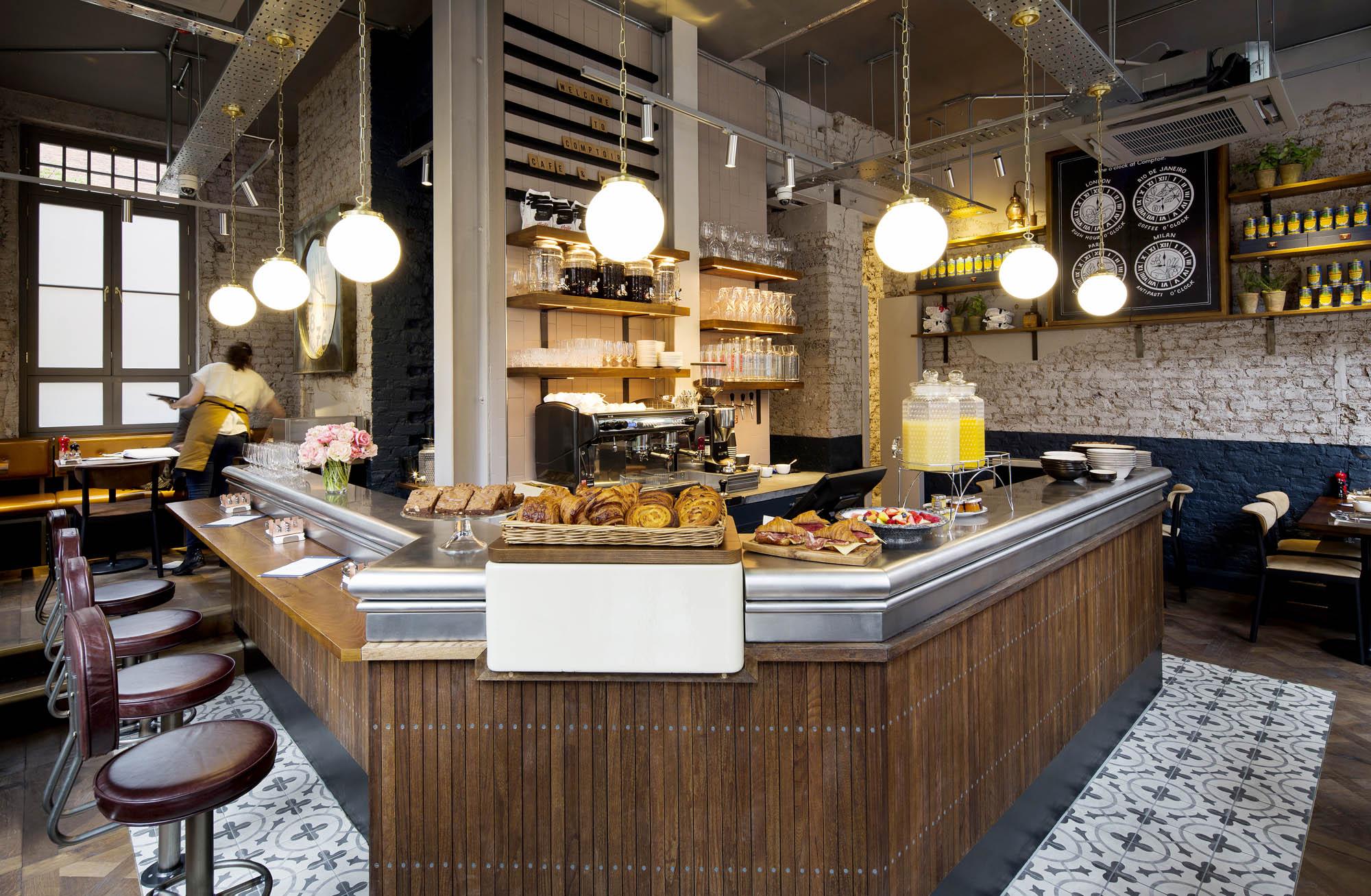 The corner coffee bar at Comptoir, with pastries on the zinc counter and globe pendants above
