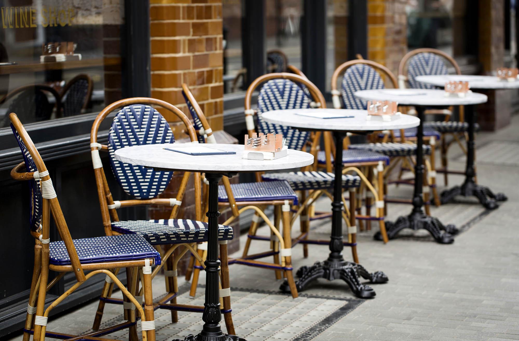 Marble bistro tables and cane chairs on the pavement outside Comptoir